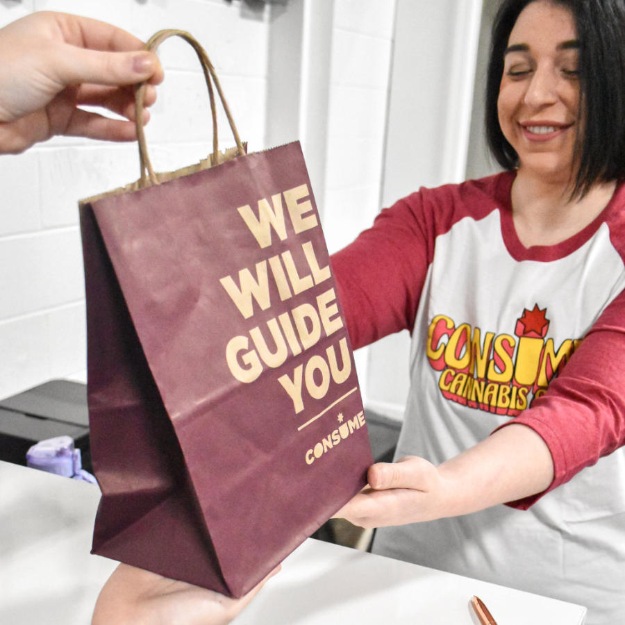 A Consume employee handing a We Will Guide You bag to a customer while wearing a Consume baseball T