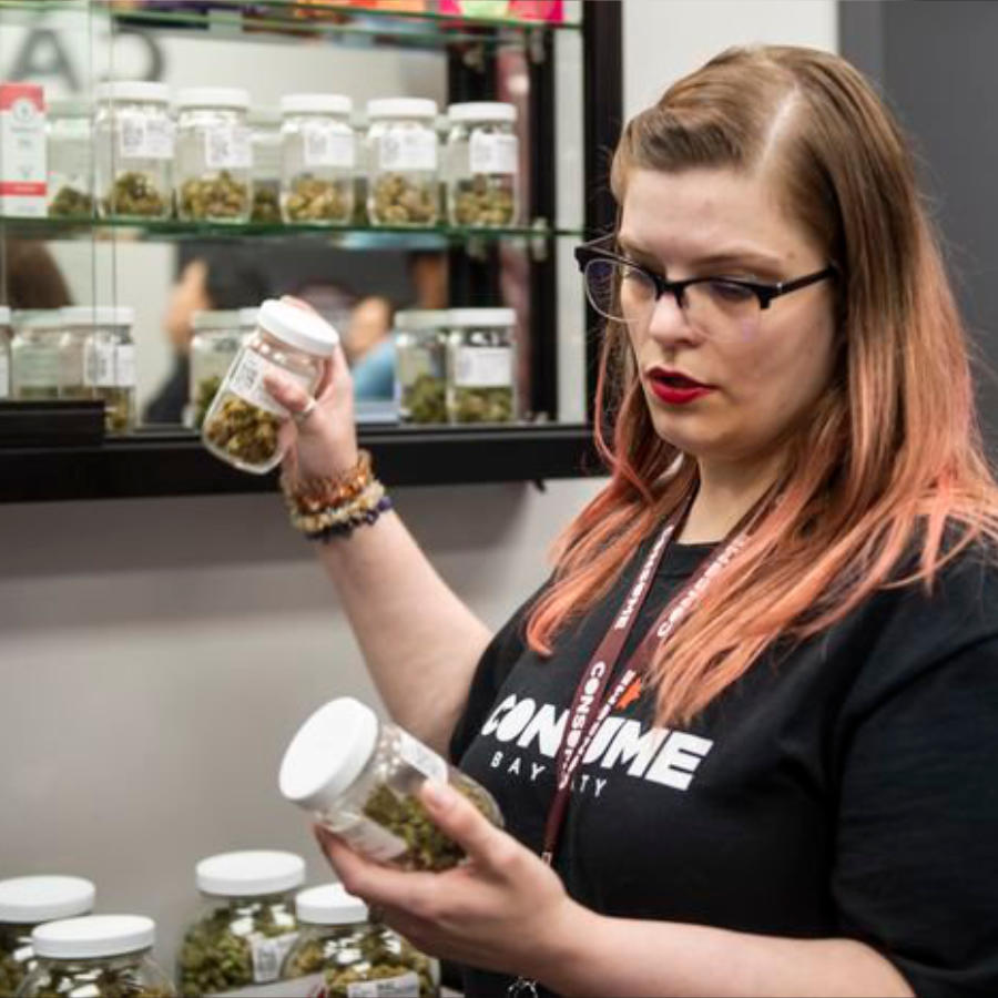 A Consume Cannabis budtender holding jars of cannabis flower