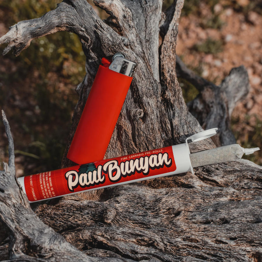 A lighter and Paul Bunyan pre-roll container resting against a tree stump, with the cannabis pre-roll sticking out of the container.
