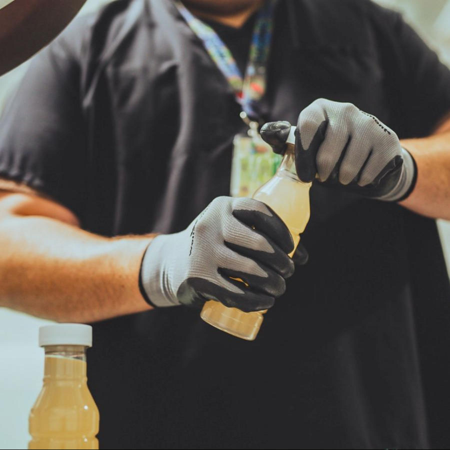 A PTS employee in a black shirt wearing a lanyard with gloves on opening a bottle of Tonic, a cannabis-infused flavored water.